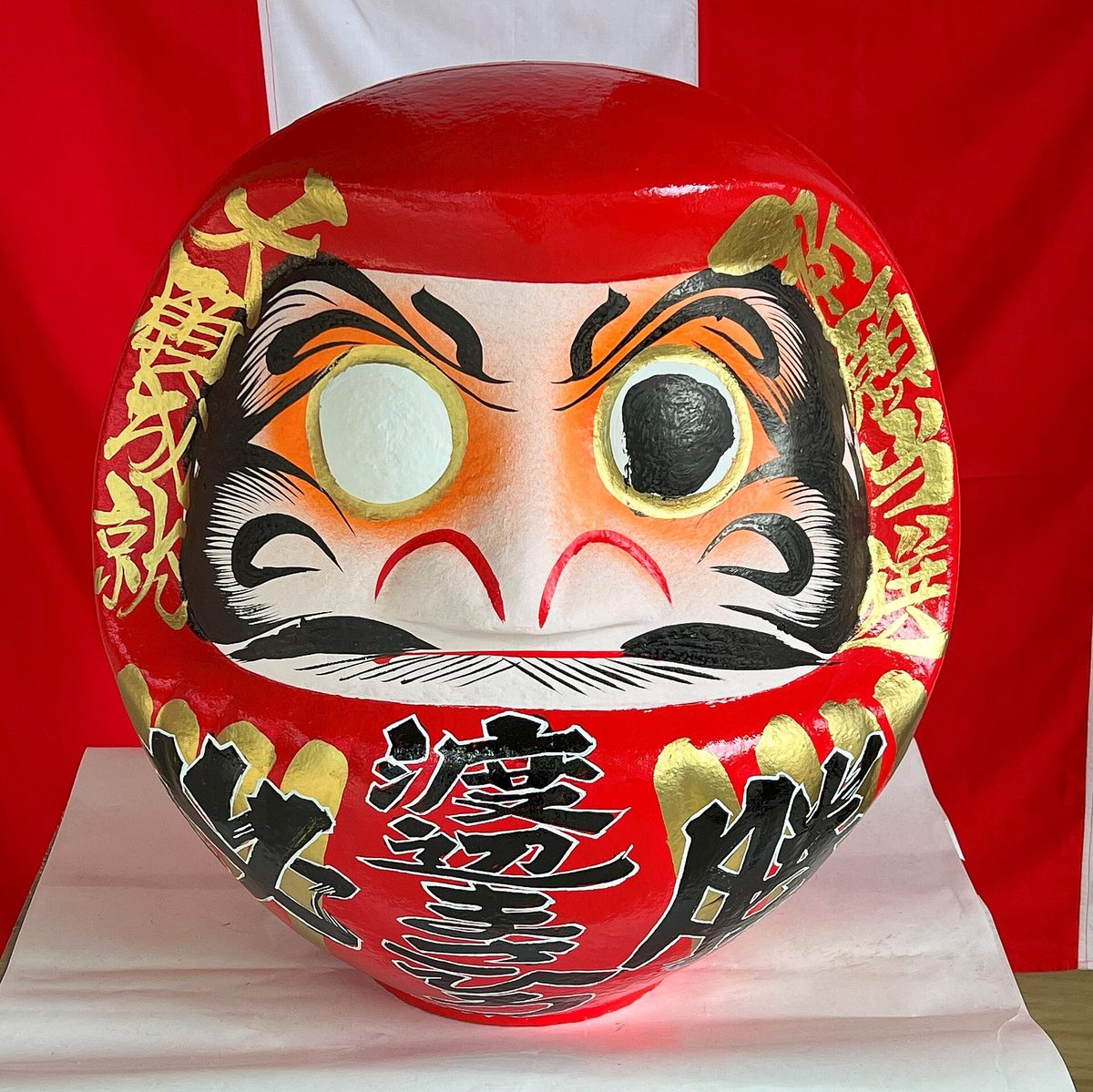 A red Takasaki daruma with one eye painted black and the other eye still blank white