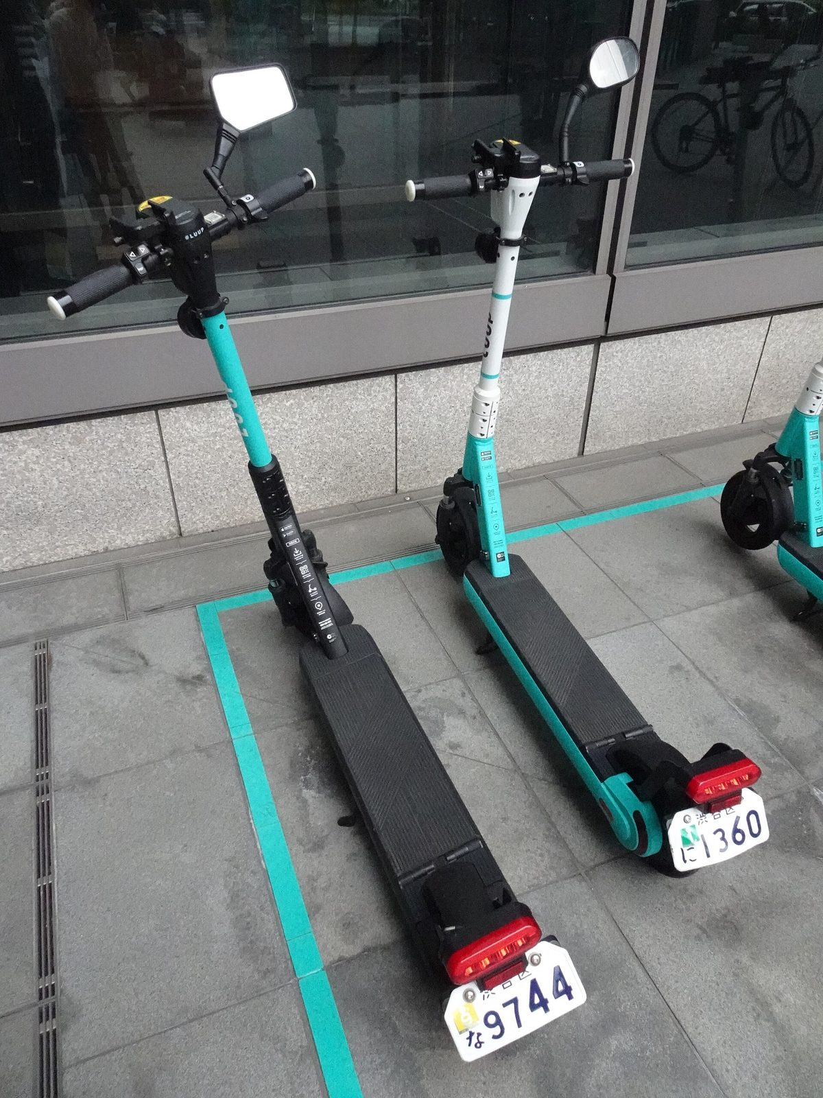 Two shared electric kick scooters parked inside a marked parking port on a sidewalk