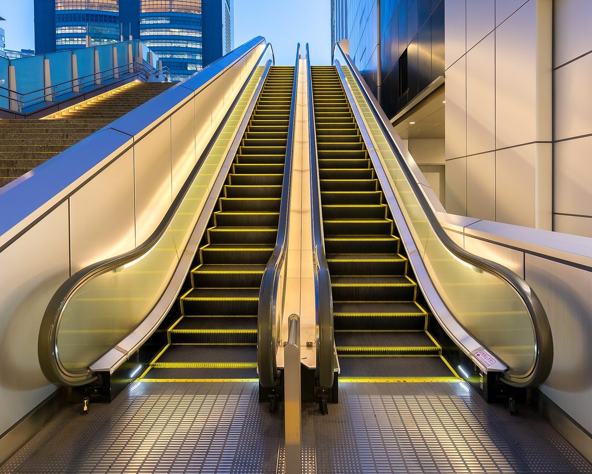 An empty two-person escalator with yellow step edges and moving handrails on both sides, at Shinjuku Station