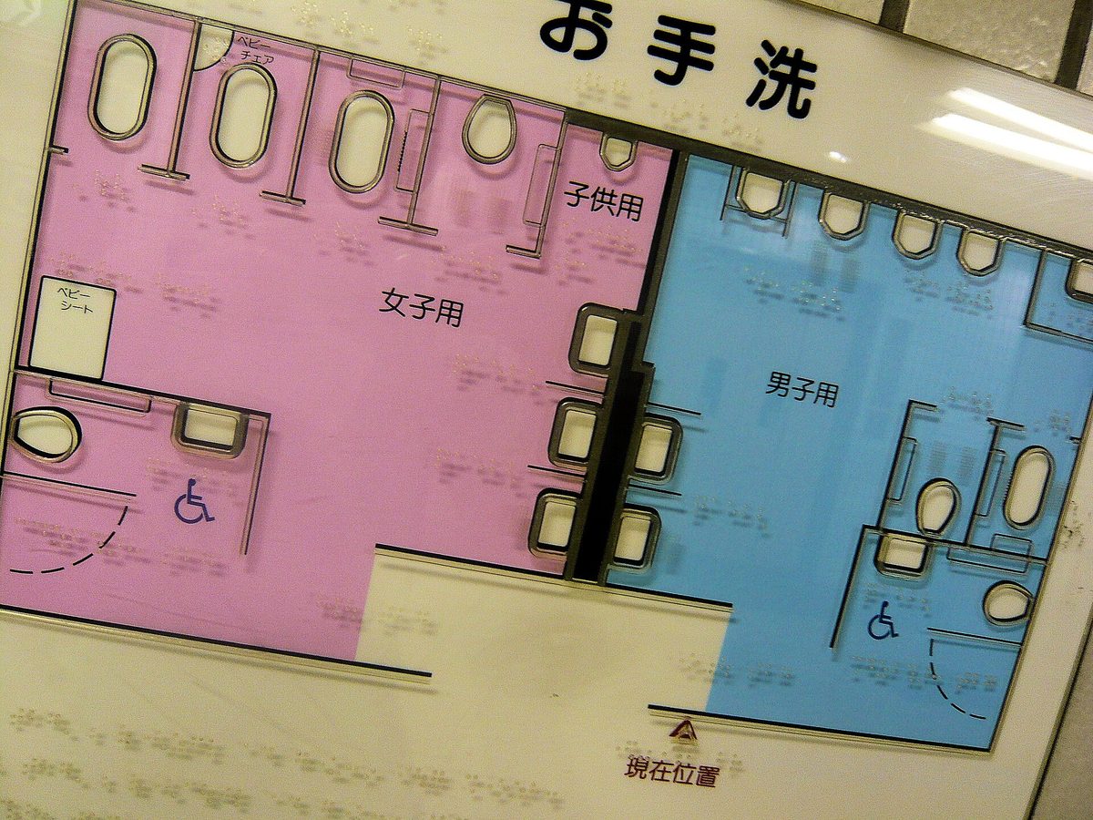 A tactile floor plan of a public toilet with pink women's and blue men's sections, headed with the Japanese word otearai
