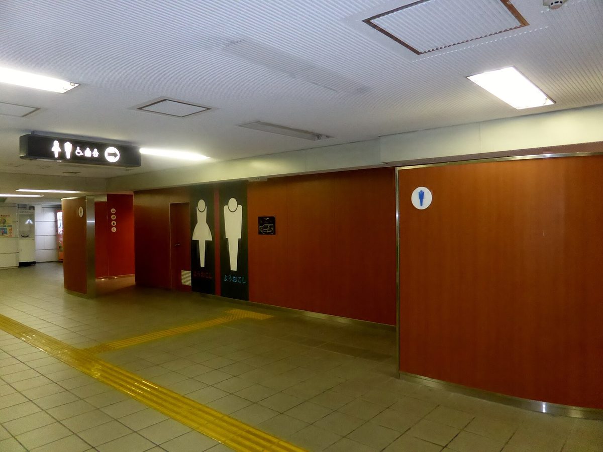 A station concourse with yellow tactile paving leading to toilet entrances marked with men's and women's pictograms