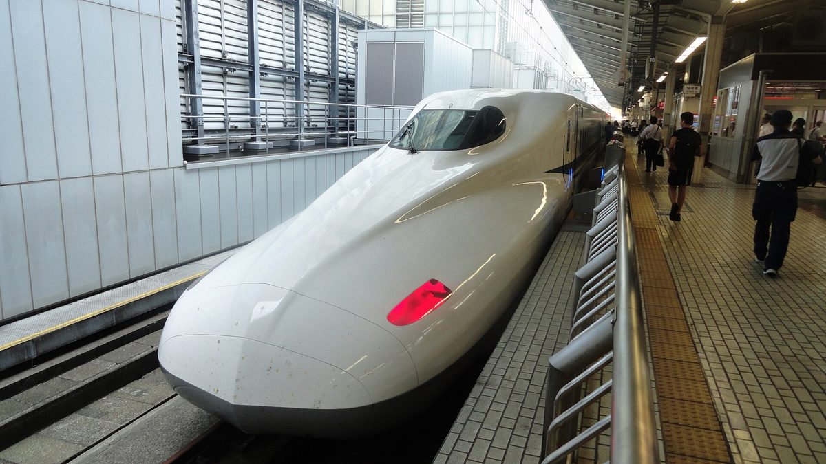 A white N700-series Shinkansen train with a long nose stopped at a platform at Kyoto Station