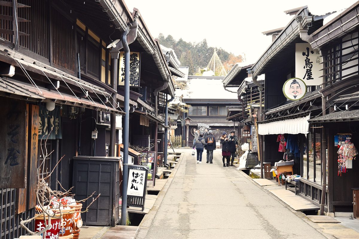 A street in the old town of Takayama (Gifu) lined with dark wooden merchant houses, shop signs and a few people walking in the distance