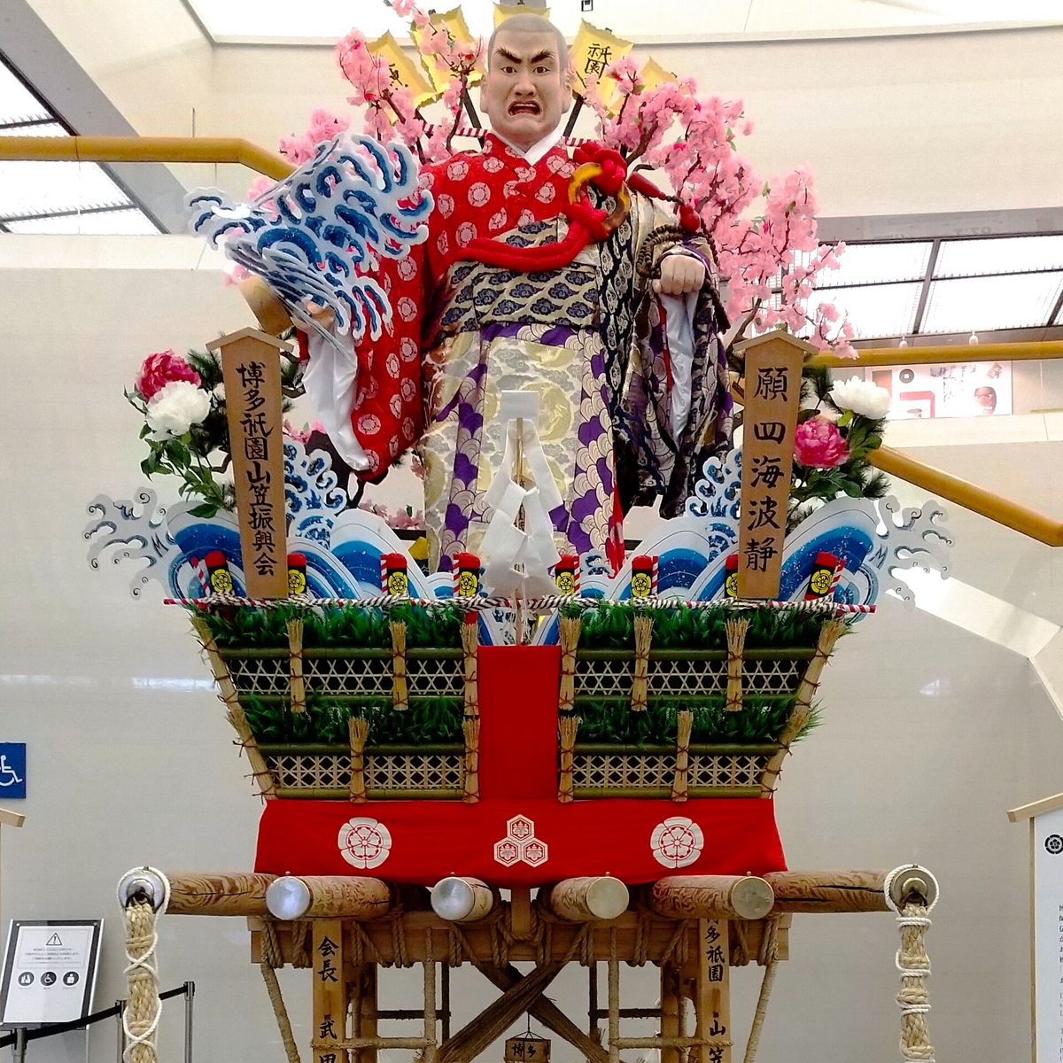 A Yamakasa festival float decorated with large traditional doll figures, on display in a museum hall
