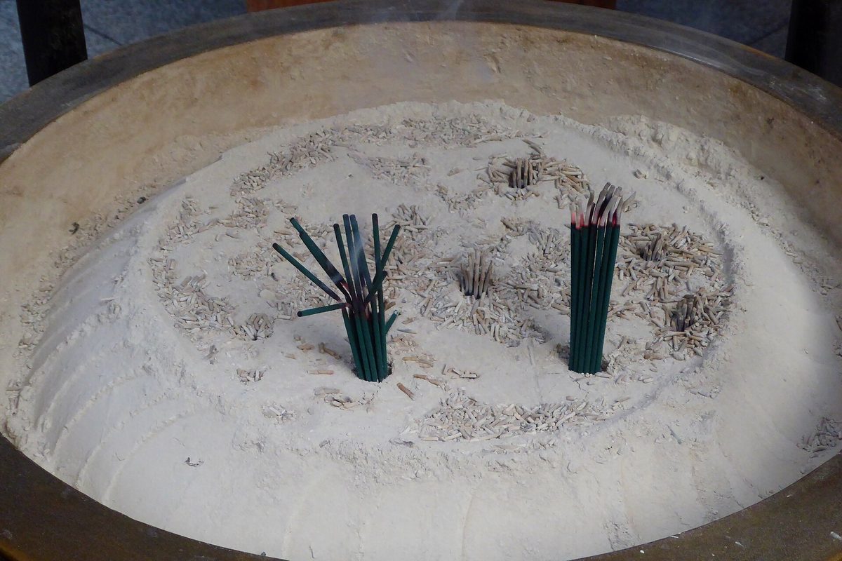 Two bundles of burning green incense sticks standing in a large round burner filled with ash