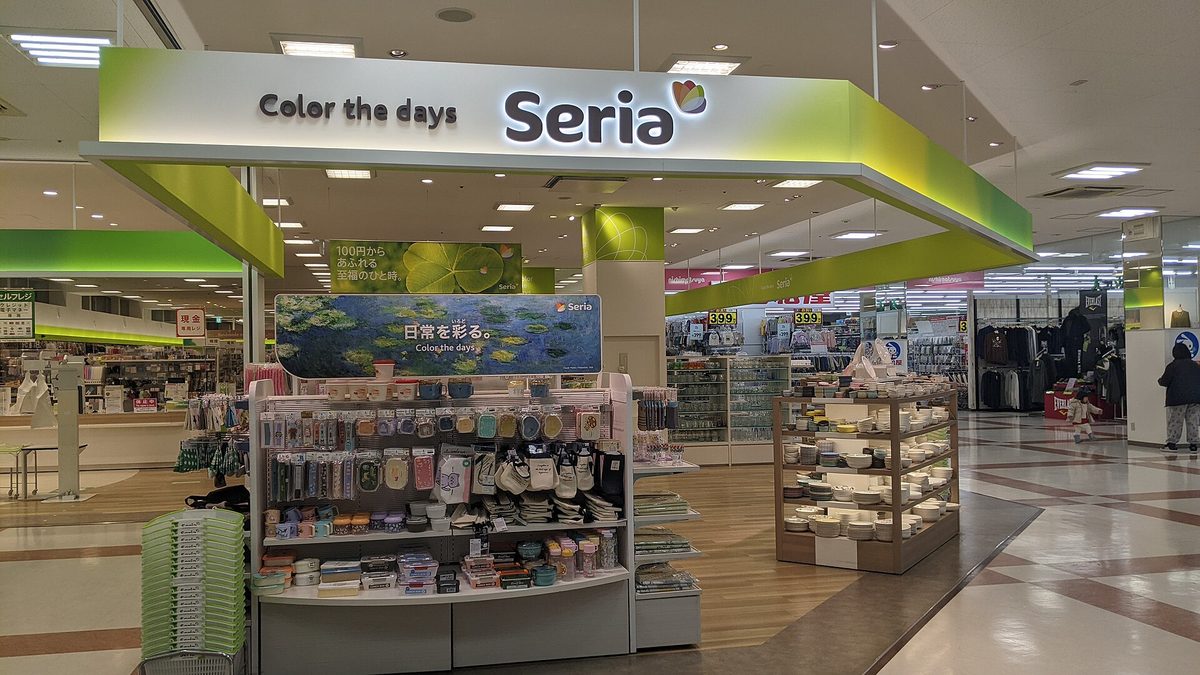 A Seria shop with a green and white sign reading Color the days Seria, with shelves of goods at the entrance
