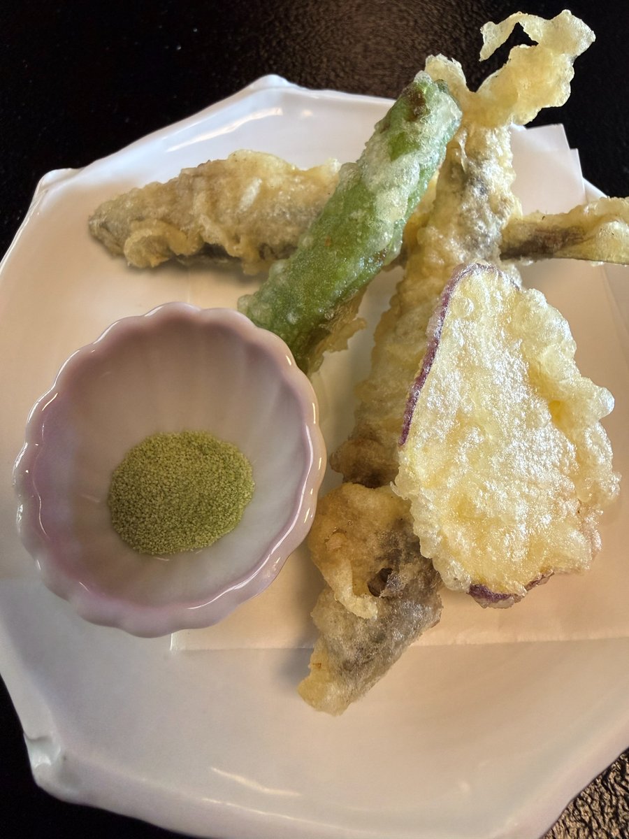 Tempura of small fish and vegetables, including a green pepper and a slice of sweet potato, on a white plate with a small dish of green matcha salt