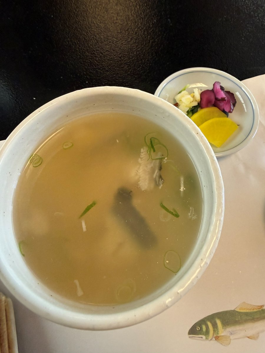 A white bowl of light rice porridge with green onion and pieces of fish, next to a small dish of pickles
