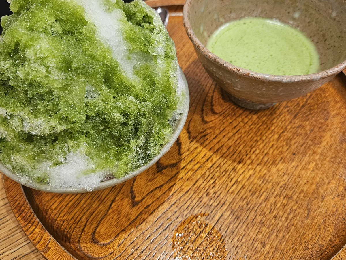 둥근 나무 쟁반 위의 녹차 시럽 빙수와 거품 낸 말차 한 잔