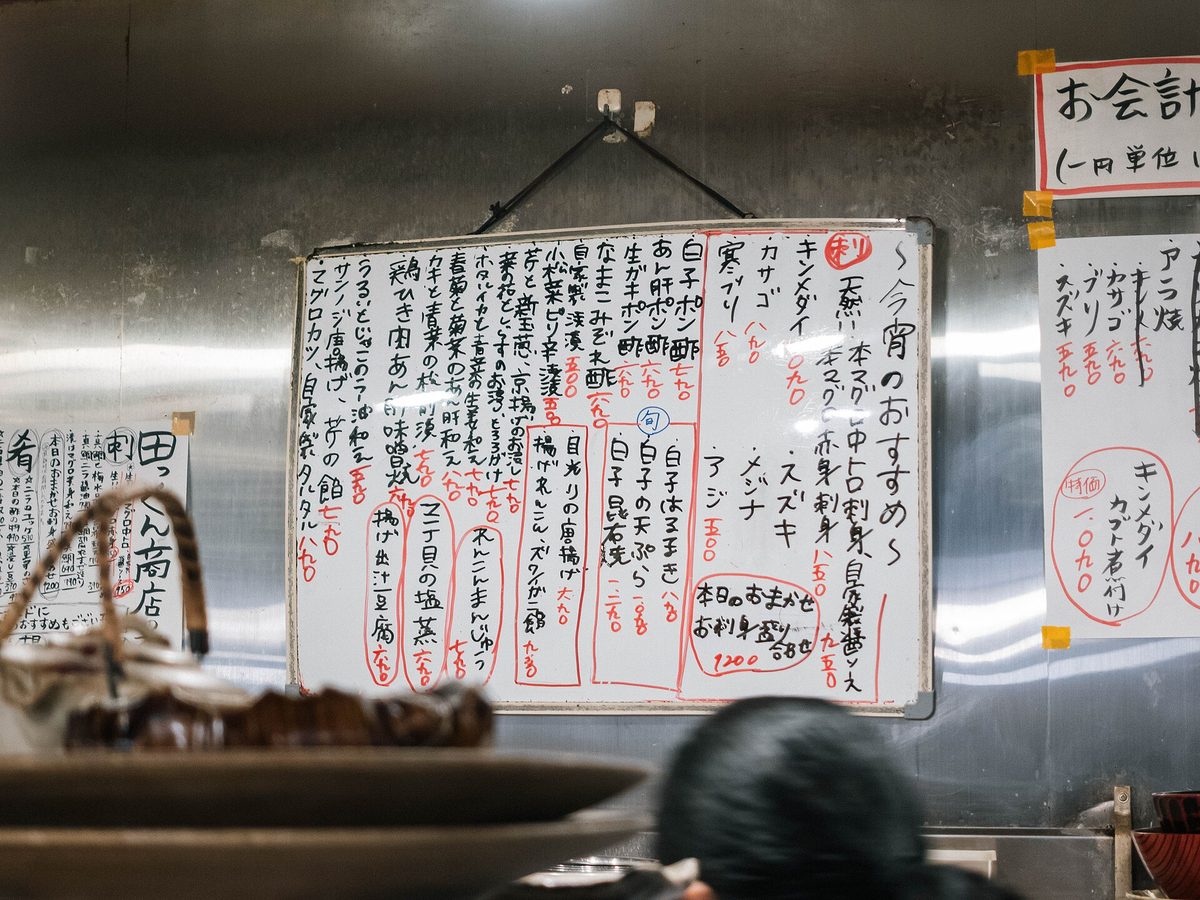 Handwritten menu sheets pinned on the wall above an izakaya counter