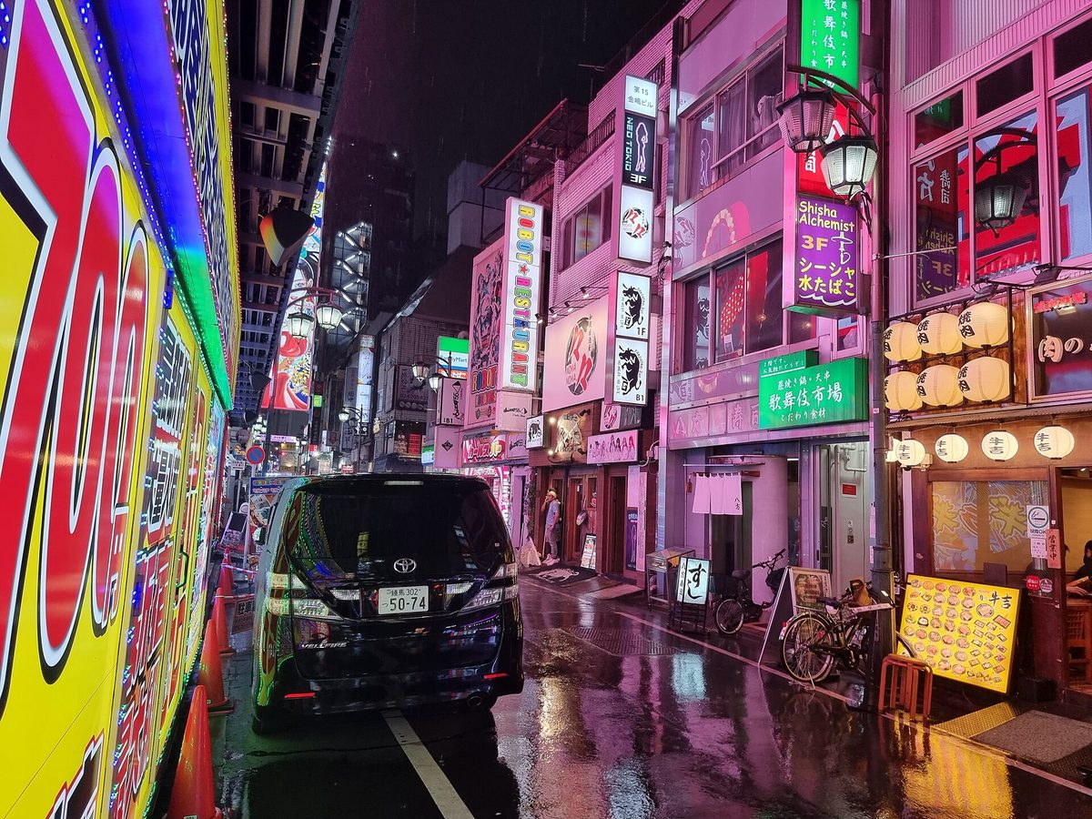 A rainy night street lined with neon signs