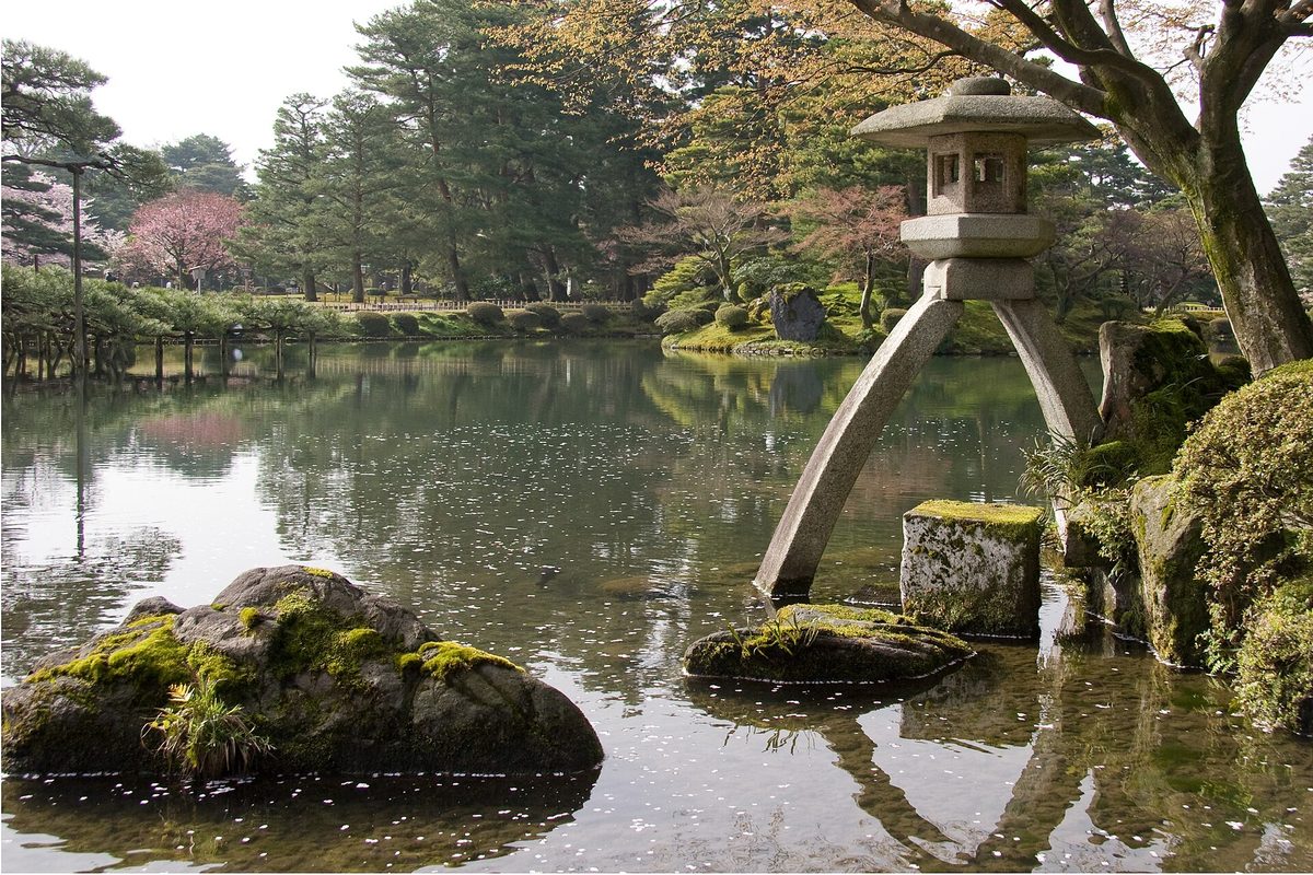 The two-legged Kotoji stone lantern standing at the edge of Kasumigaike Pond in Kenrokuen, with a pine tree and mossy rocks