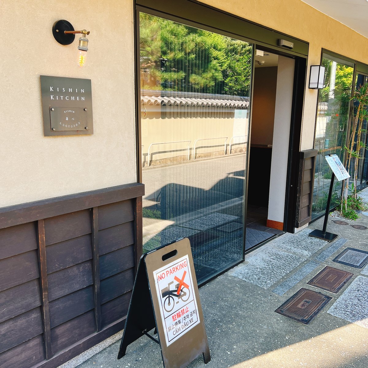 The front of a building with a glass door, a small sign reading KISHIN KITCHEN and a sign stand on the pavement