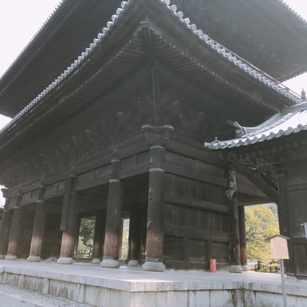 A huge two-story wooden temple gate with dark beams and tiled roofs, seen from close below