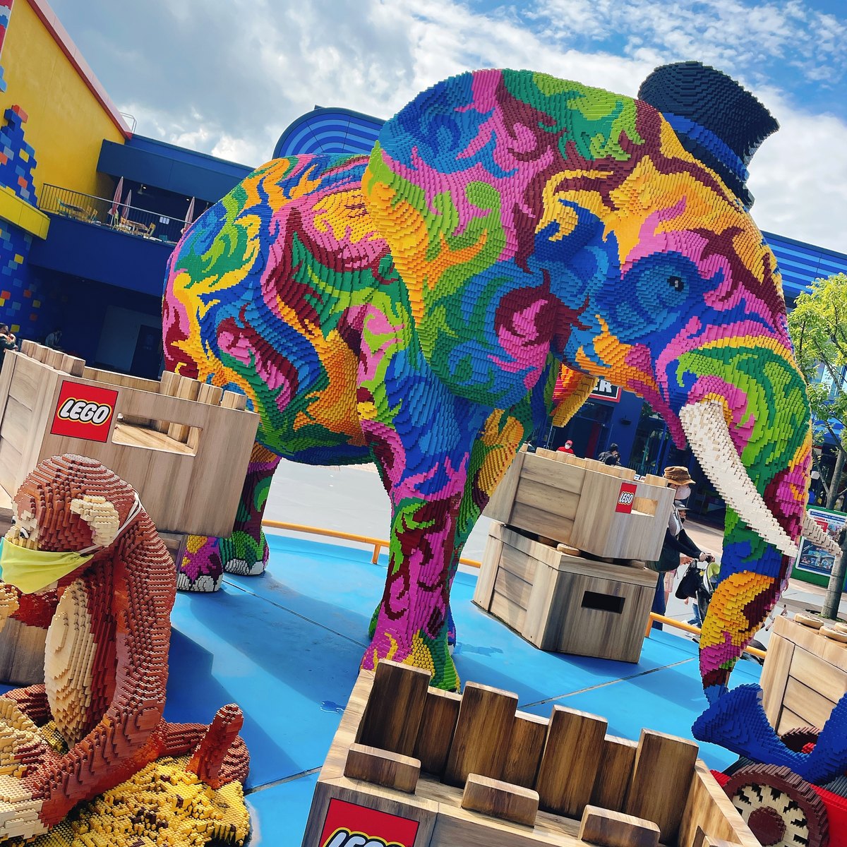 A large elephant built from LEGO bricks in many bright colors, next to LEGO crates