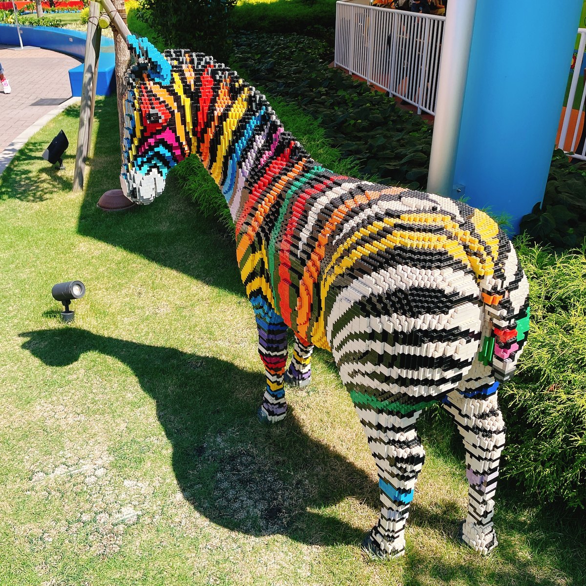 A zebra built from LEGO bricks with rainbow-colored stripes, standing on a lawn
