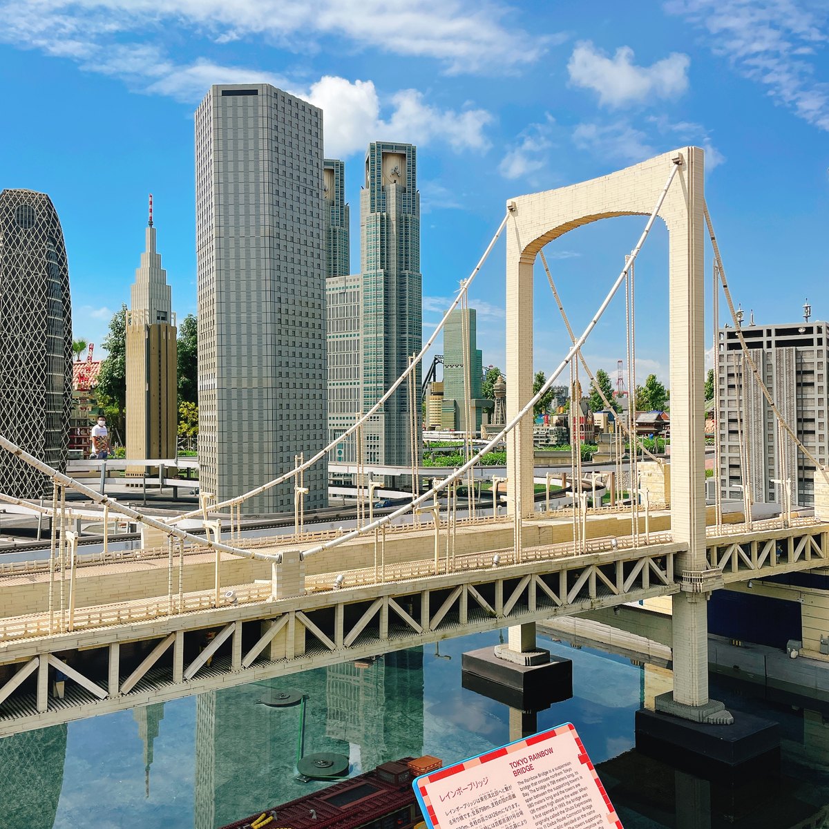 A LEGO model of a white suspension bridge and tall office towers under a blue sky