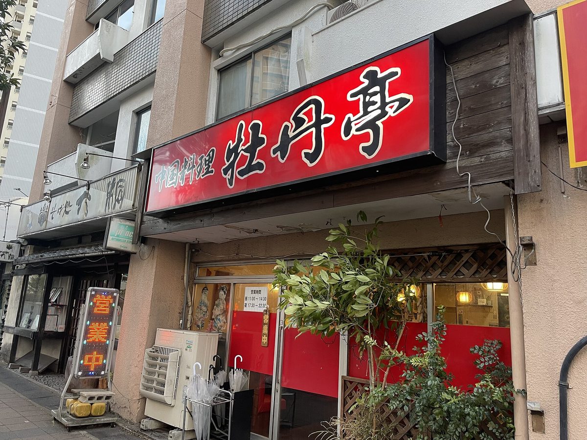 The front of a small Chinese restaurant with a big red sign and a lit "open" sign on a street in Nagoya (Aichi)