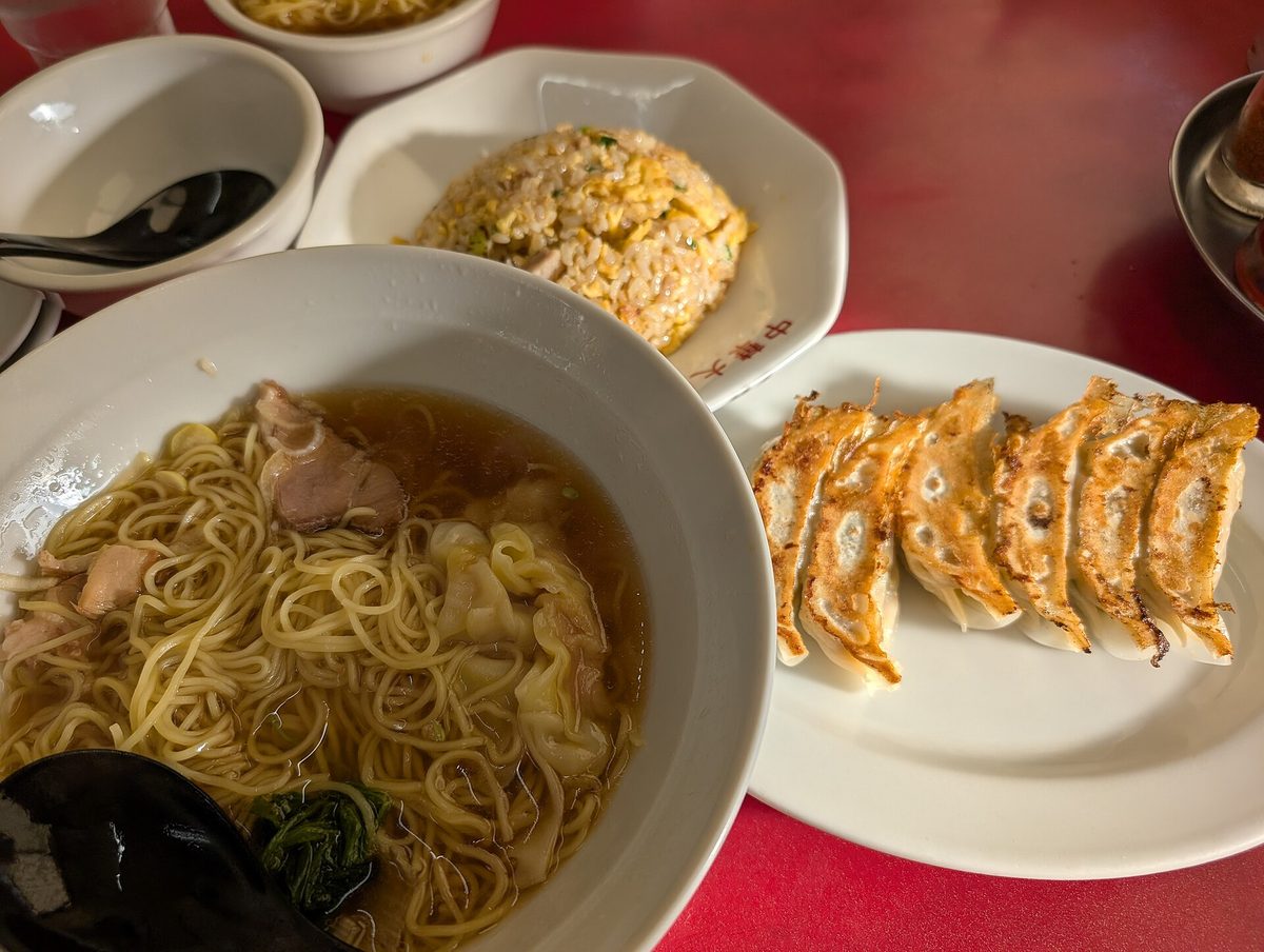 A bowl of ramen, a plate of pan-fried gyoza and fried rice served together on a table