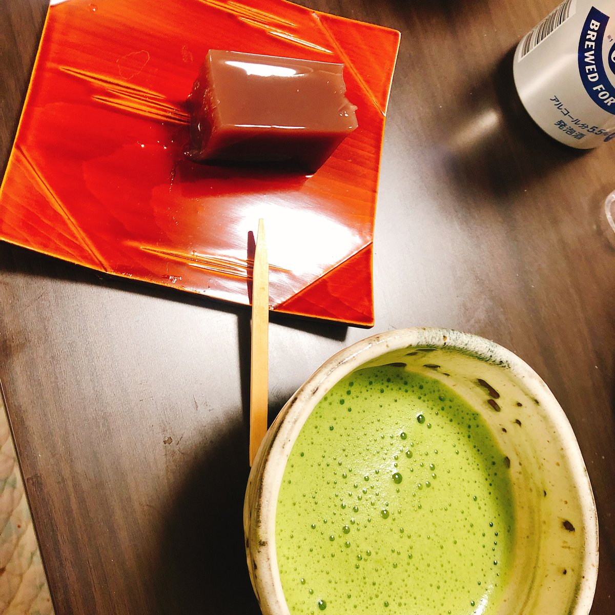 A bowl of frothy green matcha in front of a slice of yokan, a sweet bean jelly, on a red lacquer plate