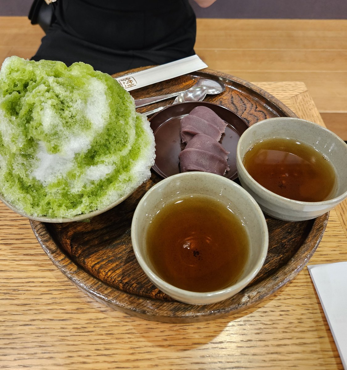 木托盤上淋著綠色抹茶糖漿的刨冰，旁邊有一小碟紅豆餡和兩個小杯