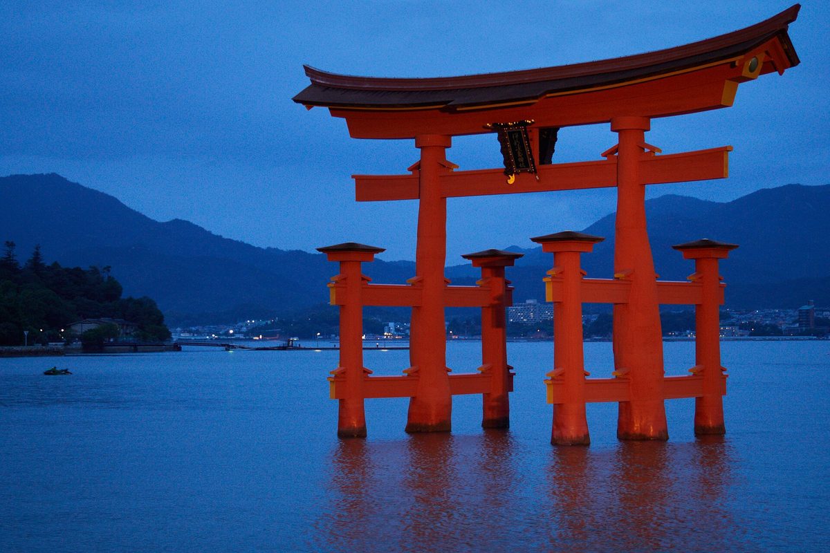 The red torii gate of Itsukushima Shrine standing in the sea at dusk