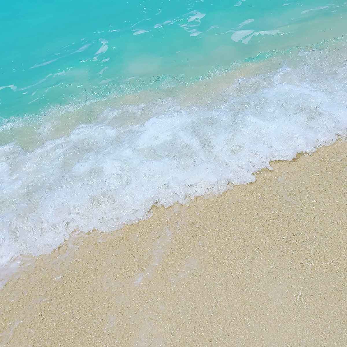 Clear turquoise water and white foam washing up on pale sand