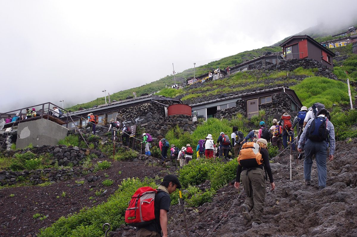 Climbers walking up a rocky trail past mountain huts on Mt. Fuji