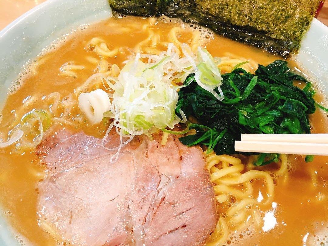 A bowl of beef-bone ramen in a creamy brown broth, topped with chashu pork, spinach, sliced green onion and a sheet of nori