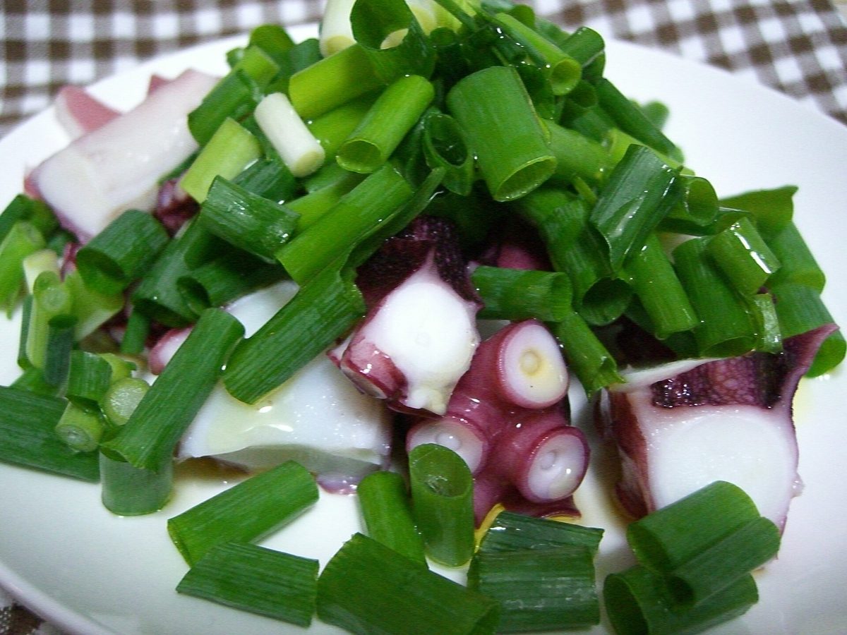 Bite-size pieces of boiled octopus with purple-red skin and white flesh, topped with lots of chopped green onion