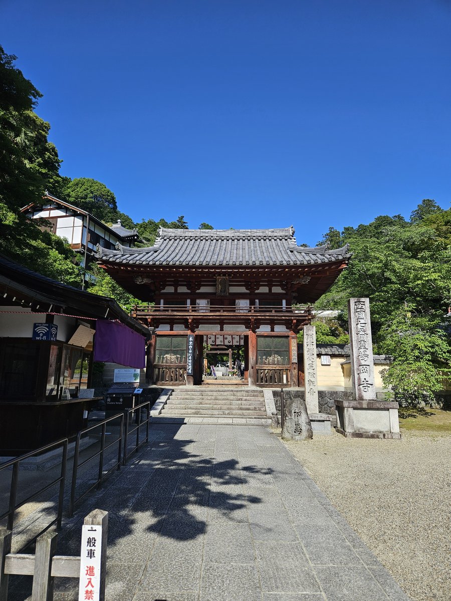 幾級石階上方的紅柱木造山門，旁邊立著高大的石柱，背景是藍天