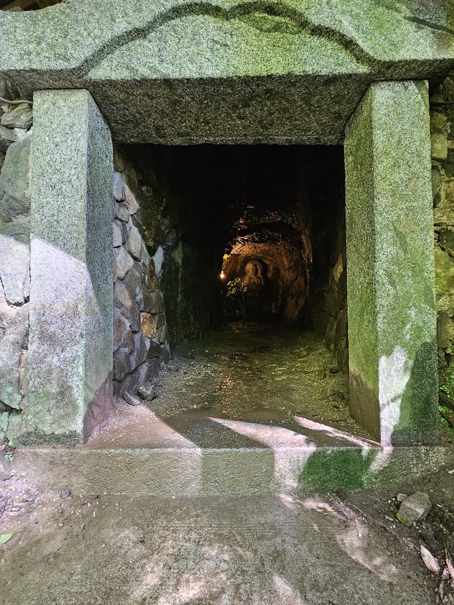 通往昏暗岩石隧道的低矮石造入口，盡頭有小燈與石造坐像