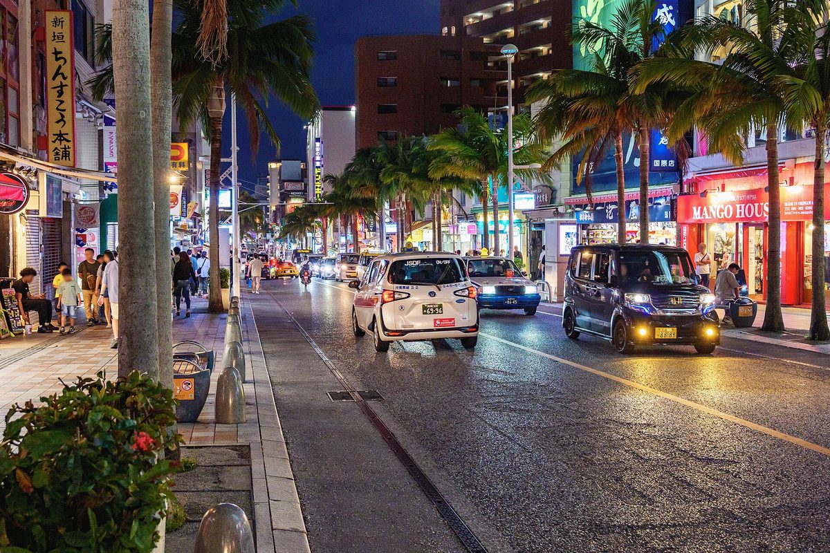 Cars driving along Kokusai-dori at dusk, with palm trees and shop lights, Naha (Okinawa)