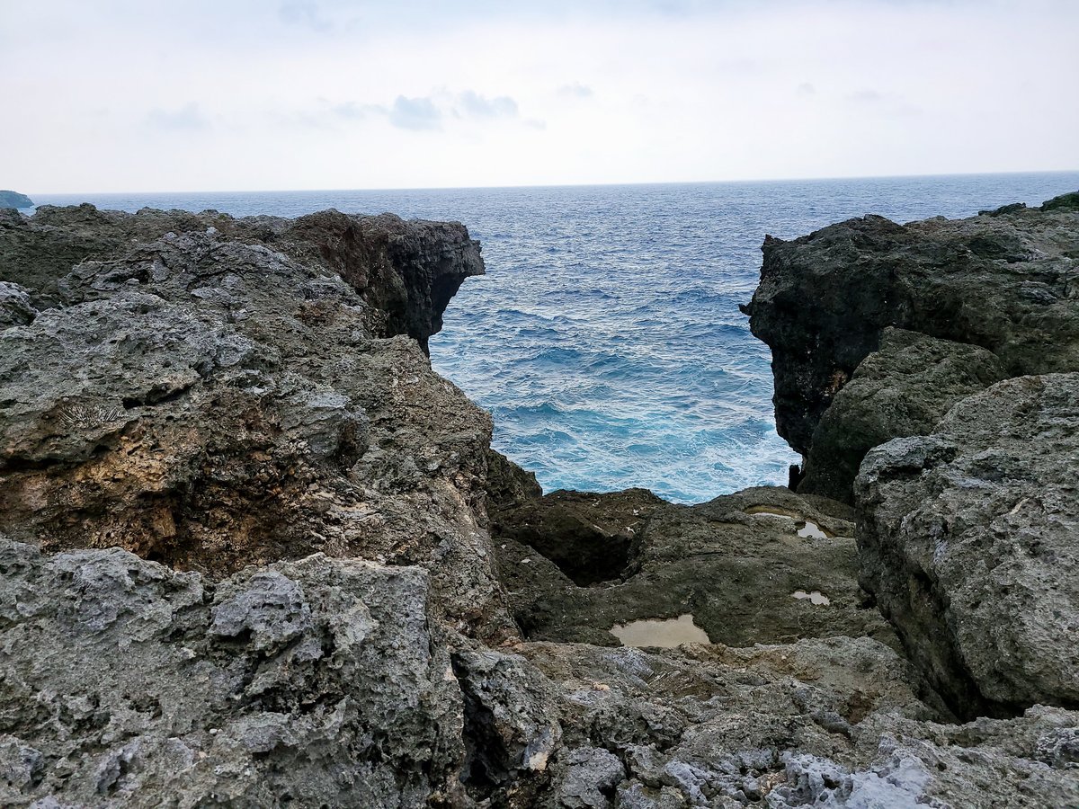 Rough gray coral rocks on the shore with a gap that opens onto deep blue sea and white waves