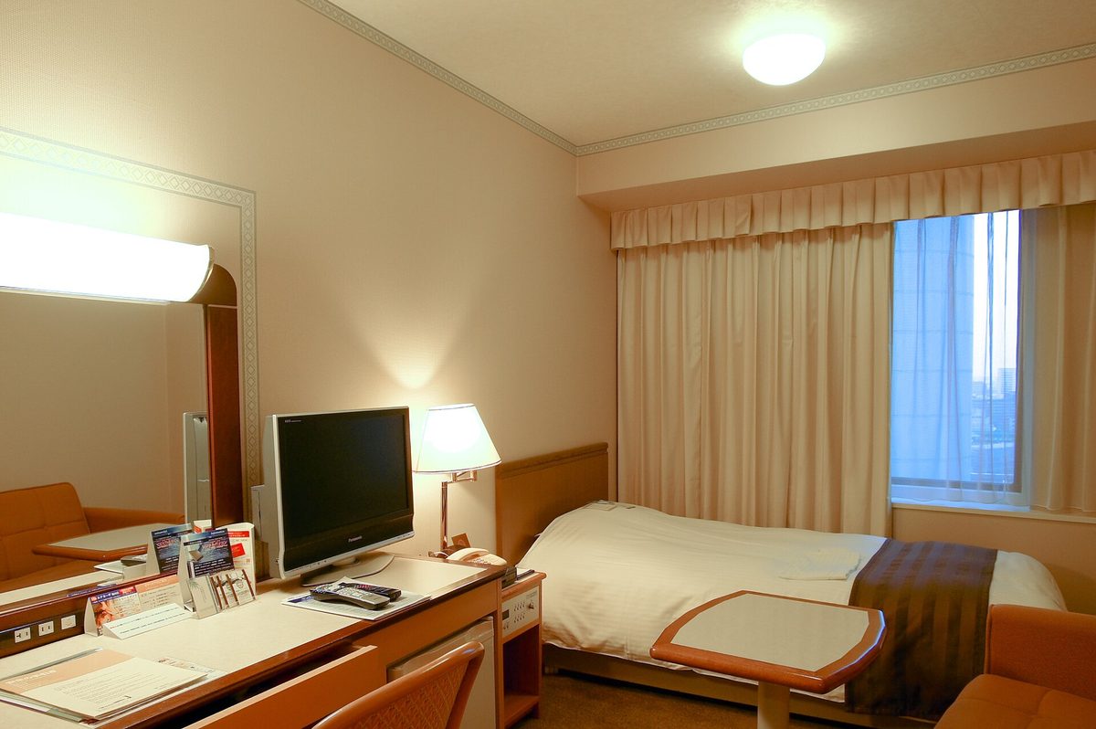 A hotel single room with a bed, a desk and a television by the window
