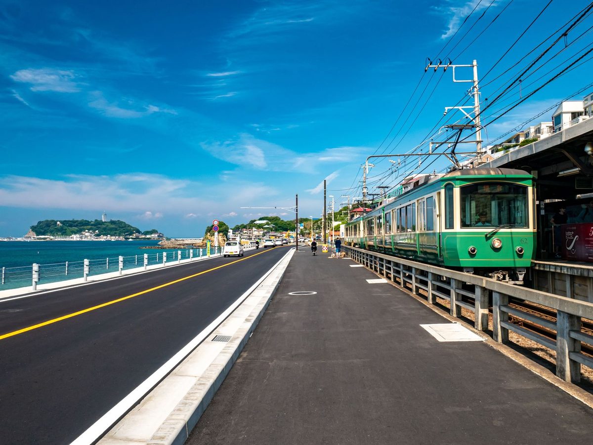A seaside road and a green tram at a small station platform under a blue sky