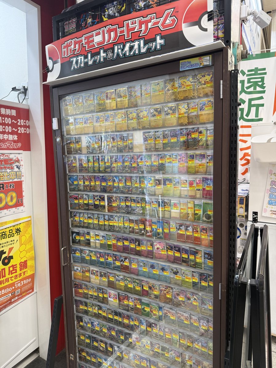 A tall glass case full of single Pokémon cards in sleeves, each with a yellow price tag, under a Pokémon Card Game sign