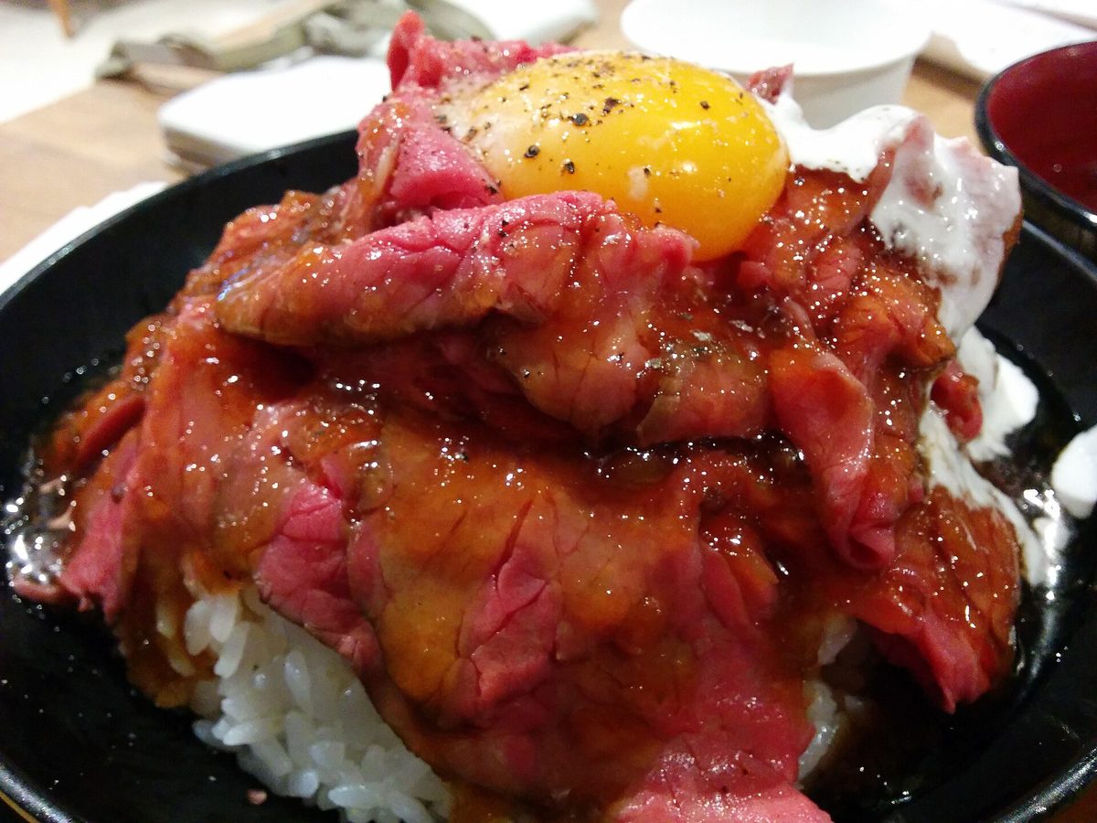 A Japanese roast beef bowl: thin pink slices of beef piled over rice, topped with a raw egg yolk