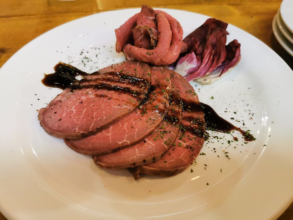 Slices of roast beef on a white plate, brown at the edge and pink all the way through