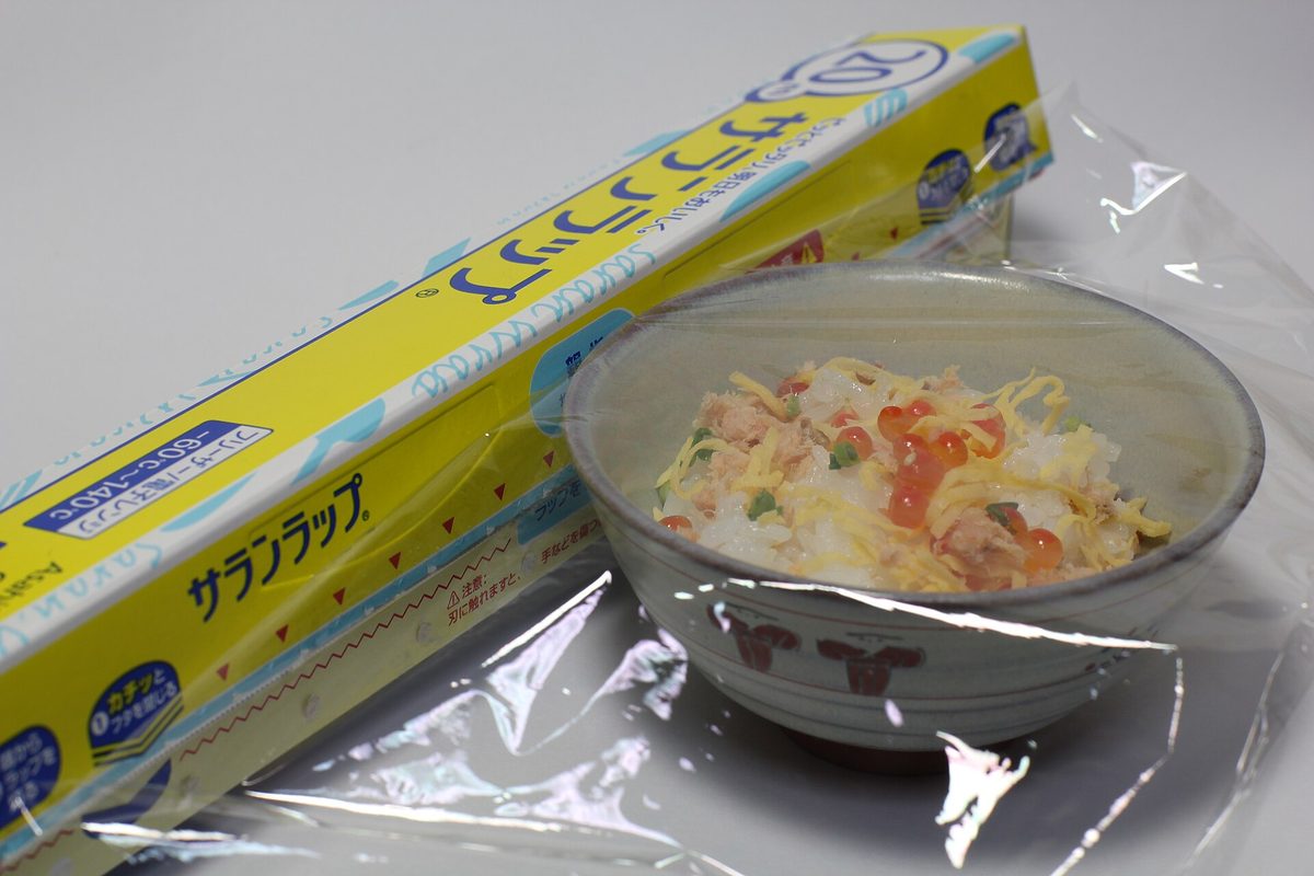 A box of Saran Wrap with a sheet of clear film pulled out beside a bowl of rice