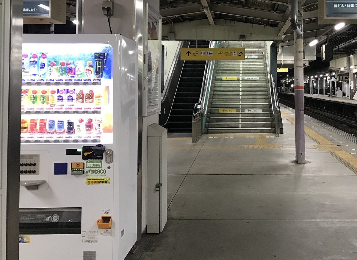 A brightly lit drink vending machine standing on a train station platform in Japan