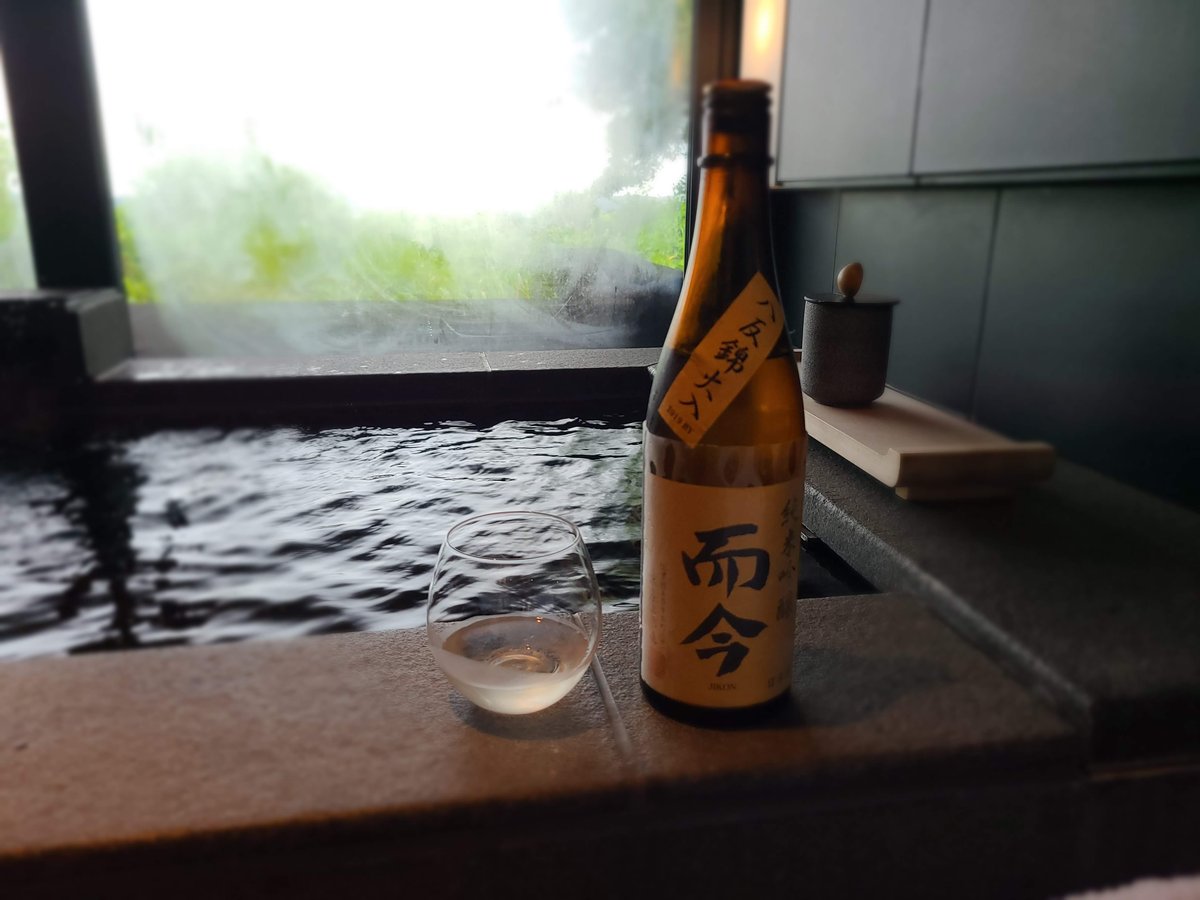 A bottle of Jikon sake and a small glass on the edge of a private hot-spring bath, with trees outside the window