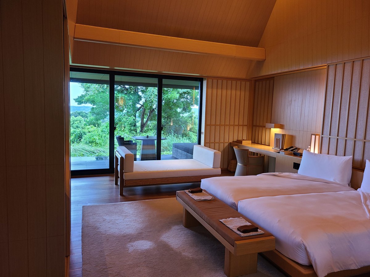 A spacious suite with two beds, a low wooden table and large windows onto green trees