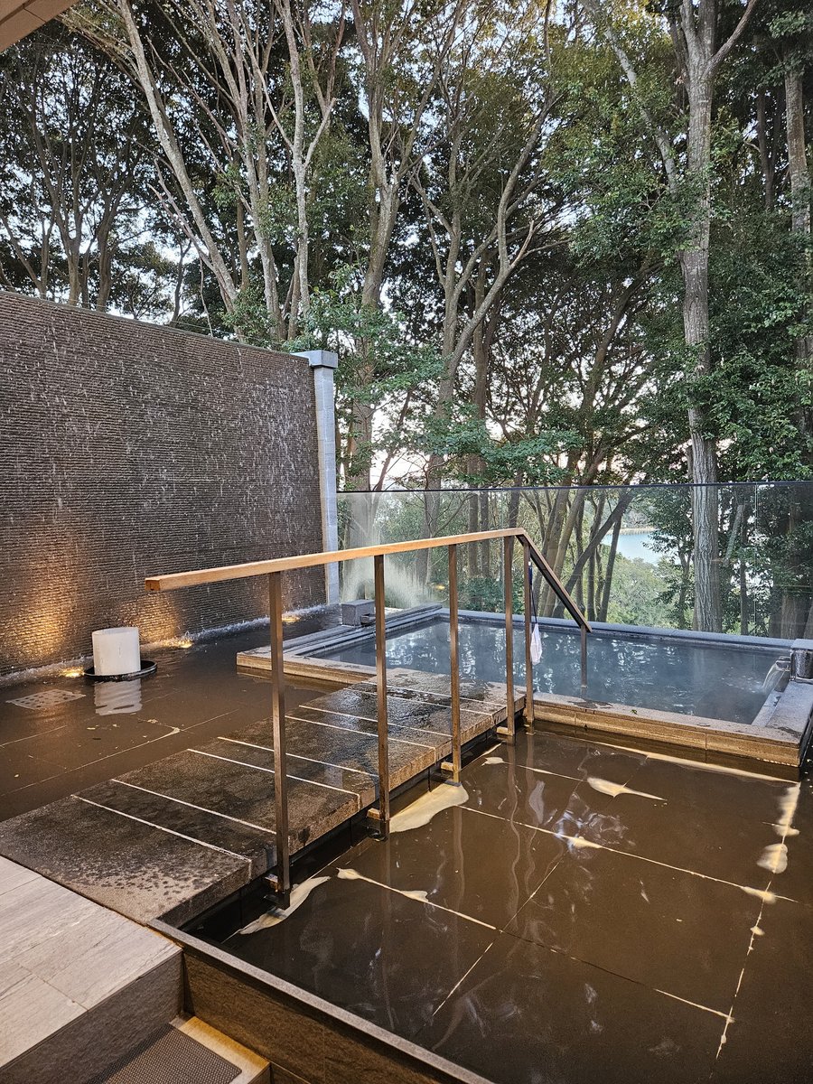 An open-air bath on a stone terrace looking out over trees and the sea