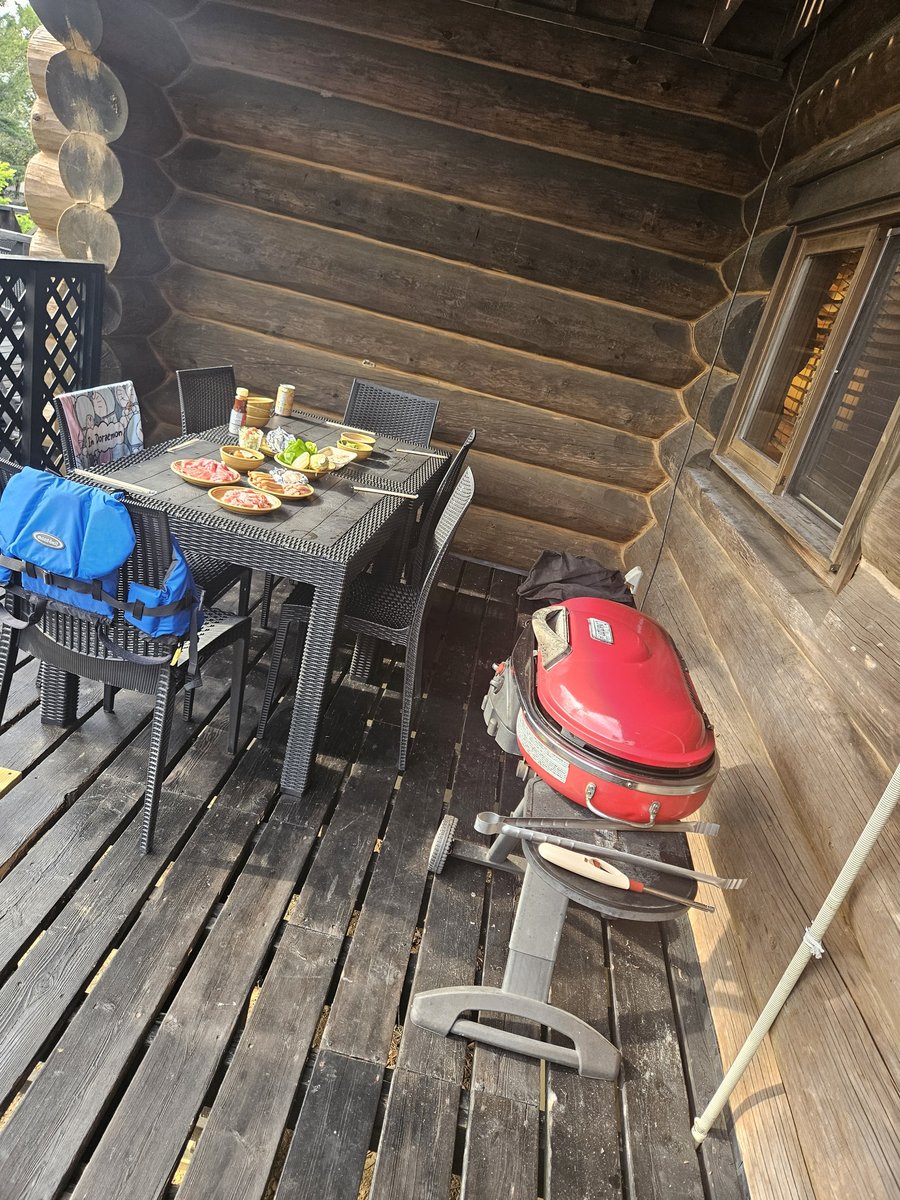 A red gas grill and a table set with food on the wooden terrace of a log cabin