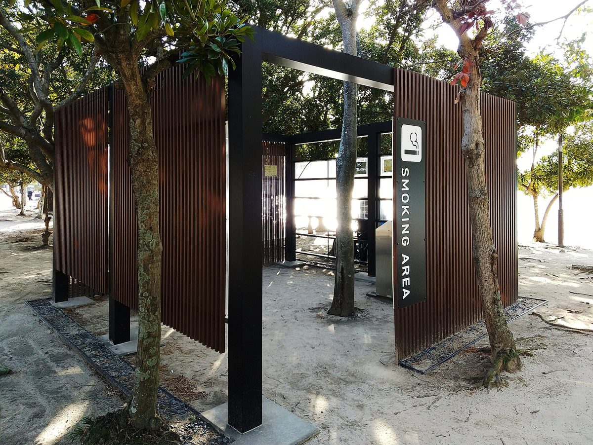 An outdoor designated smoking area enclosed by dark wooden screens in a park
