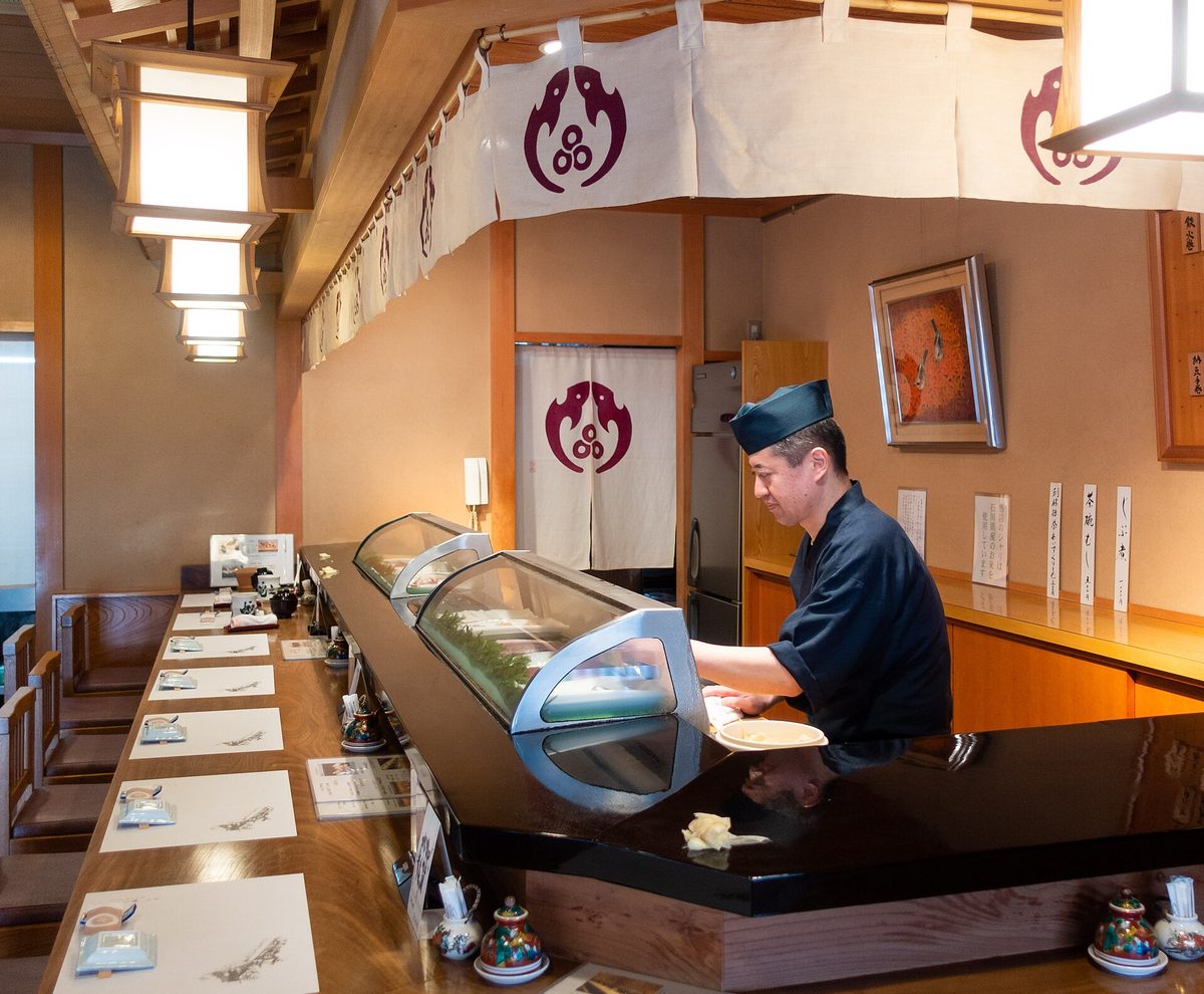 A sushi chef working behind a long wooden counter in a sushi restaurant