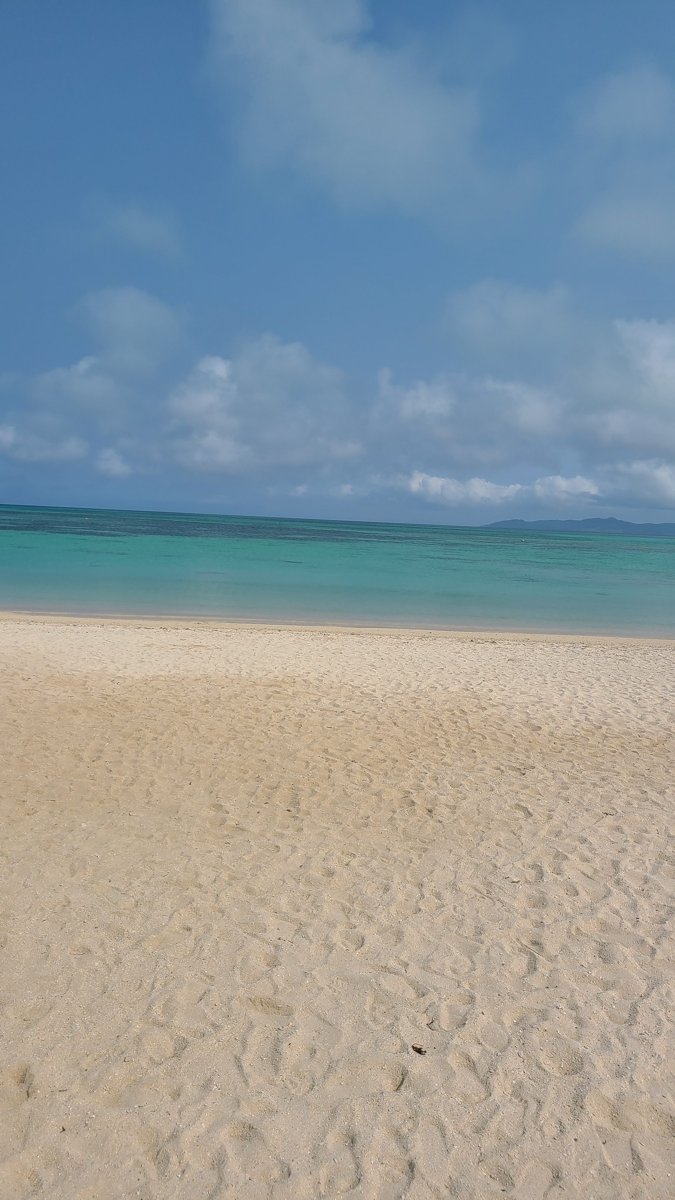 A wide beach of pale sand leading to shallow turquoise water and a blue sky with white clouds