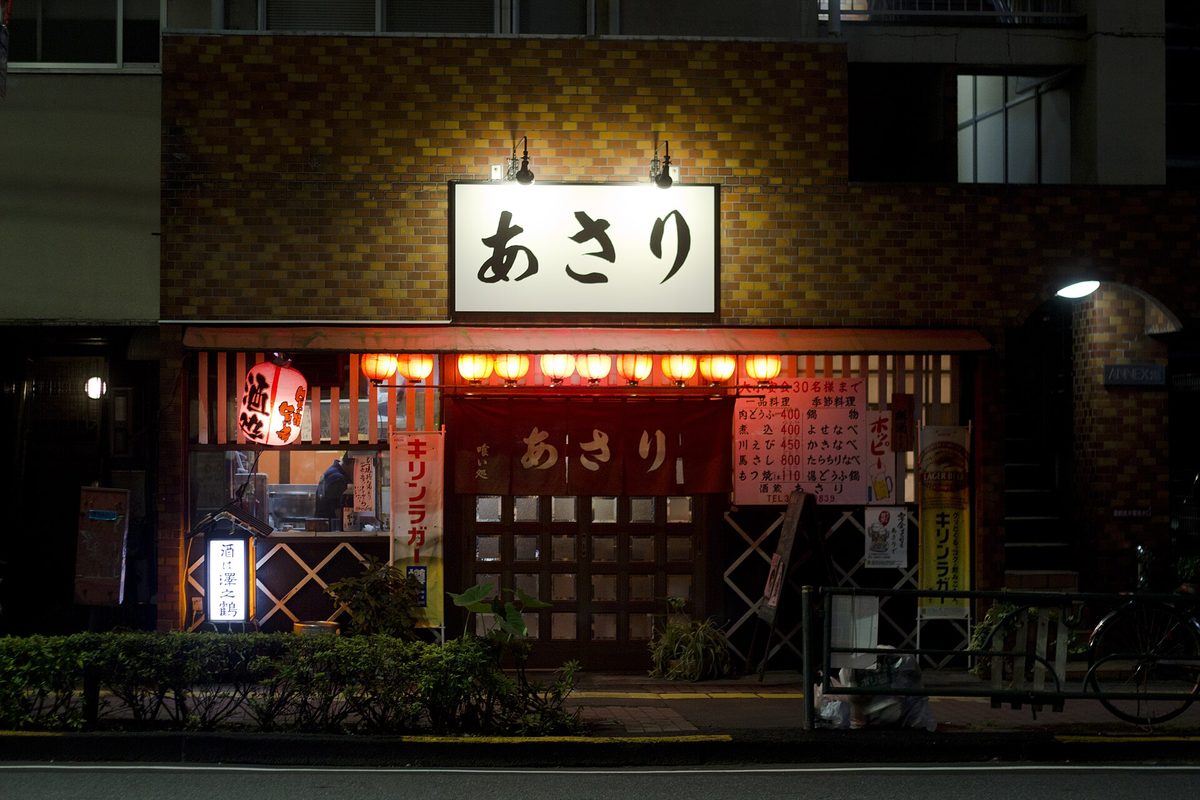 The lit entrance of a small izakaya with a white sign