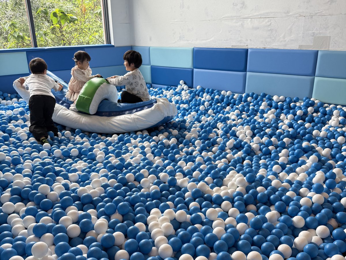 Children playing in a large ball pool full of blue and white balls, with a big inflatable toy